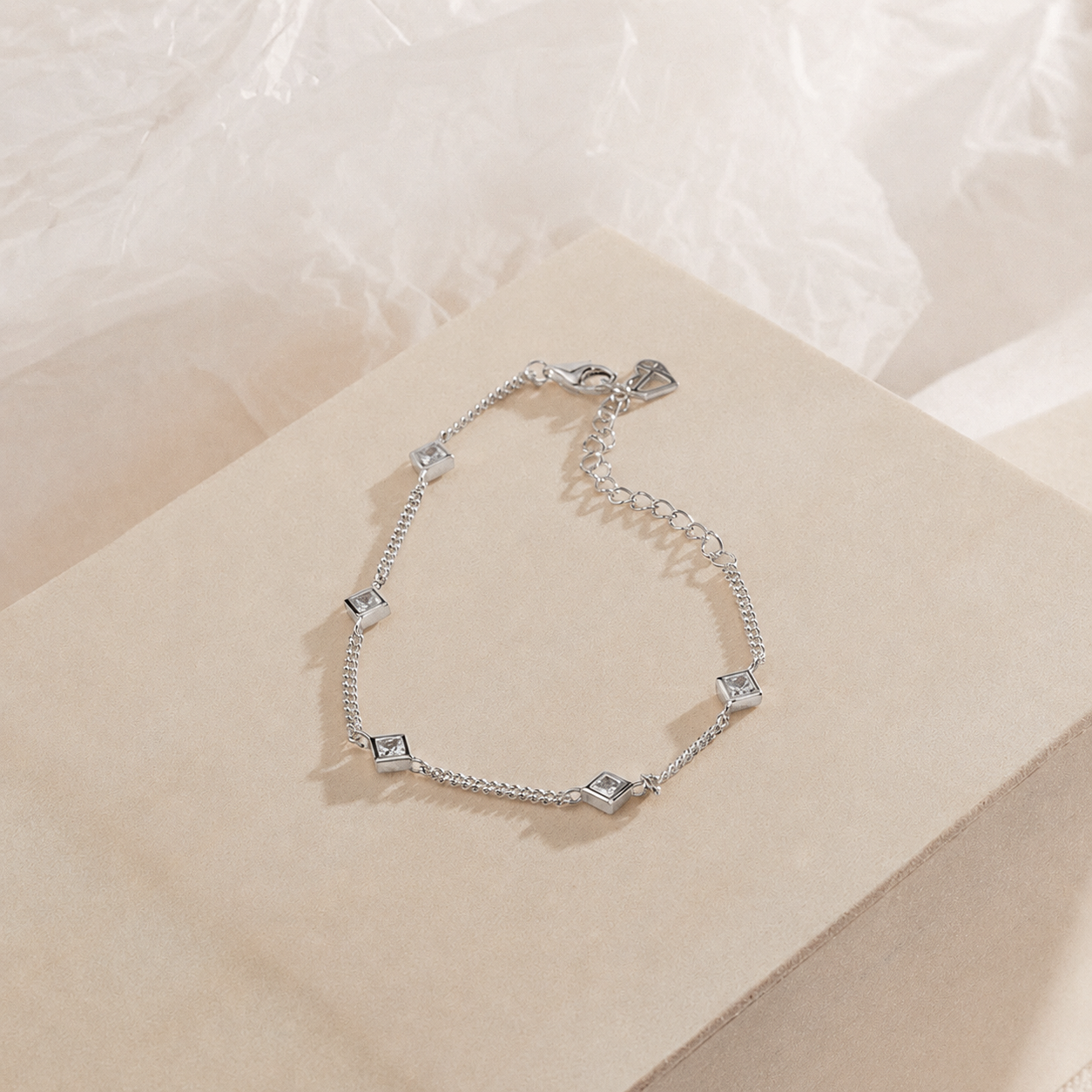 Silver bracelet with square charms on a beige surface